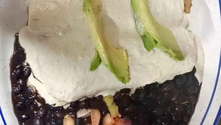 Angel's enchilada under a pale green tomatillo cream sauce with sliced avocado, on a bed of black beans