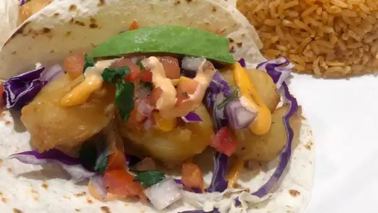 A baja shrimp taco with red cabbage, pico and avocado on a flour tortilla beside Mexican rice